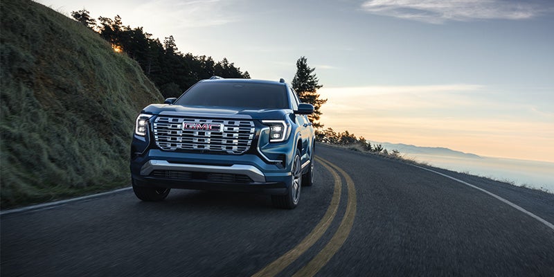 Blue GMC SUV driving on a scenic mountain road at sunset.
